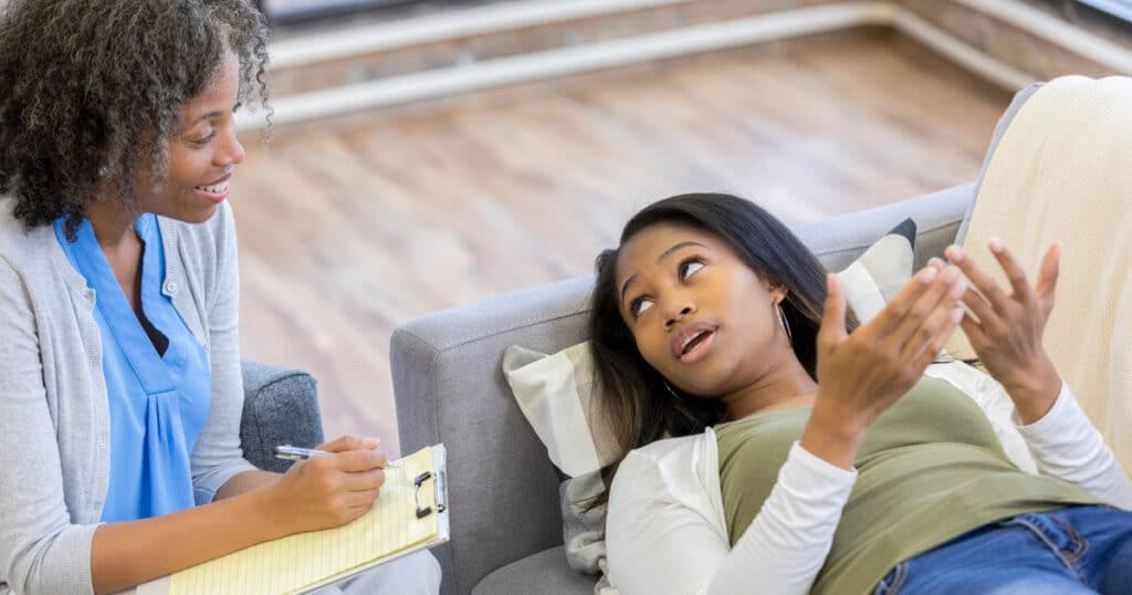 Black female mental health professional listening to patient as she lays on the couch and talks freely