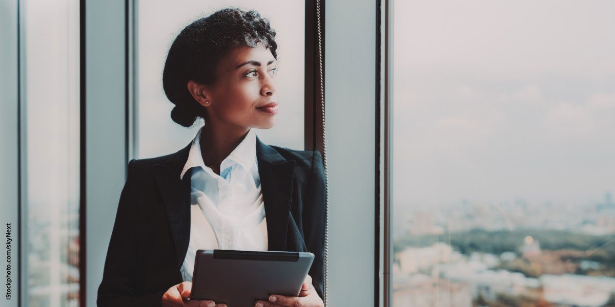 biracial businesswoman with tablet in front of office window